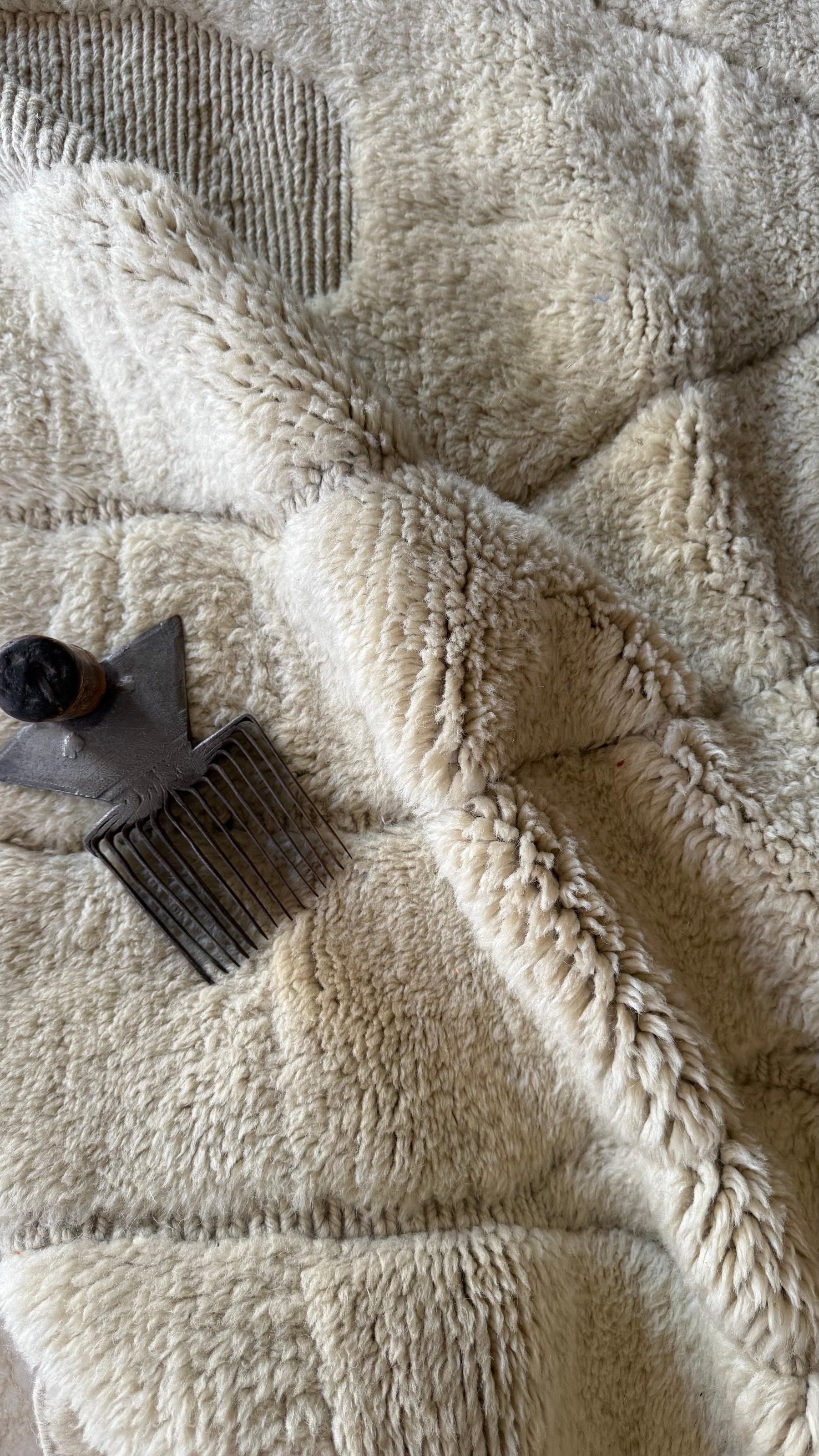 Tapis Mrirt en laine, plié, avec un peigne de tisserand posé dessus